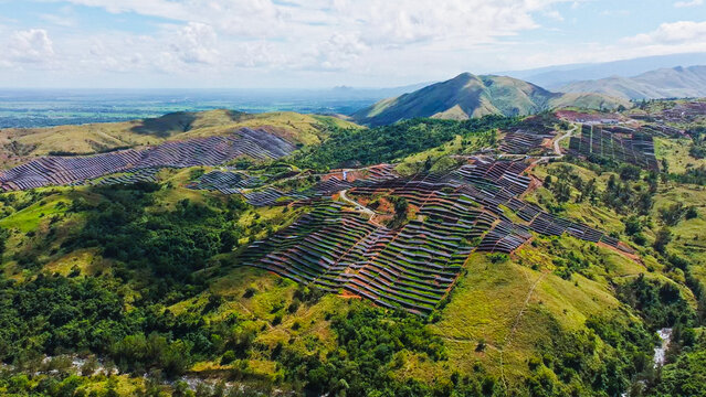 Aerial view of a large-scale solar farm integrated into the rolling green hills of a tropical landscape in Aguilar, Ilocos Region, Philippines.