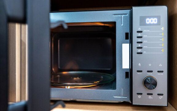 Empty microwave oven with open door. Digital timer display, mode buttons and knob on control panel. Home appliance in the kitchen