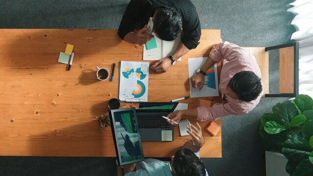 Manager talking to boss by using phone while diverse team sharing idea or financial chart in tablet. Top view of diverse people brainstorming and sharing plan while man talking to phone. Convocation.