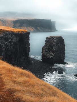 foggy coastal cliffs with a solitary sea stack above a black pebble shore and golden grass in the foreground, moody tranquil solitude