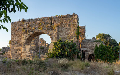 Fototapeta premium Massive ruins of ancient Great Baths with large arched openings and green thickets in historic center of resort. Side, Antalya, Turkey.
