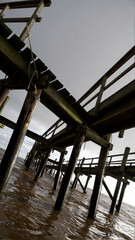 Fototapeta premium Low angle view of old wooden pier structure over muddy water under cloudy sky