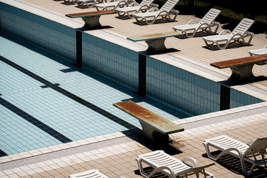 Empty swimming pool with starting blocks and sun loungers on a sunny day