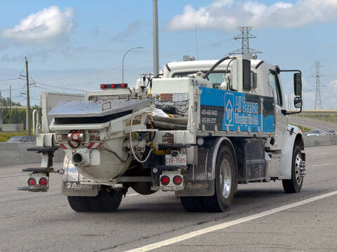 Calgary, AB, Canada. August 16, 2026. Rear three-quarter view of a white concrete pumper work truck driving along a multi-lane highway.