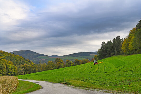 Modern tractor mowing green grass on a sloping meadow for hay production in Lower Austria