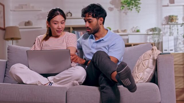 Couple on sofa with laptop at home in living room, woman and man in casual conversation, relaxed teamwork, online planning, cozy apartment interior