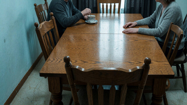 Couple sitting at wooden dining table having coffee, quiet conversation, domestic scene