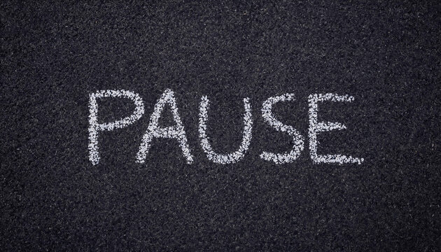 The word pause written in white chalk on a dark asphalt texture background