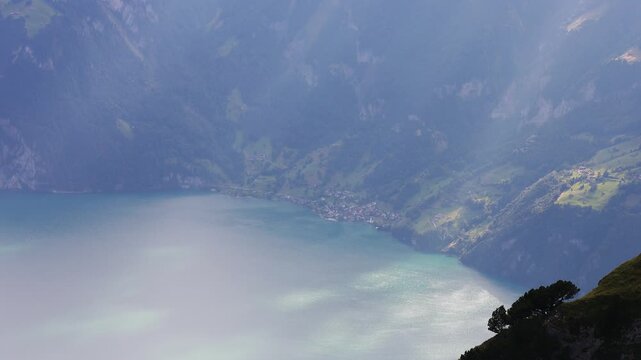 Lake Lucerne seen from the Klingenstock ridge near Stoos, Switzerland. Static shot of turquoise water far below, a lakeside village and steep forested slopes in the Swiss Alps in hazy summer