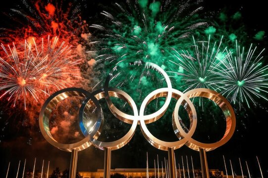 five interlocking golden rings monument at night with red and green fireworks bursting overhead, festive triumphant celebration atmosphere