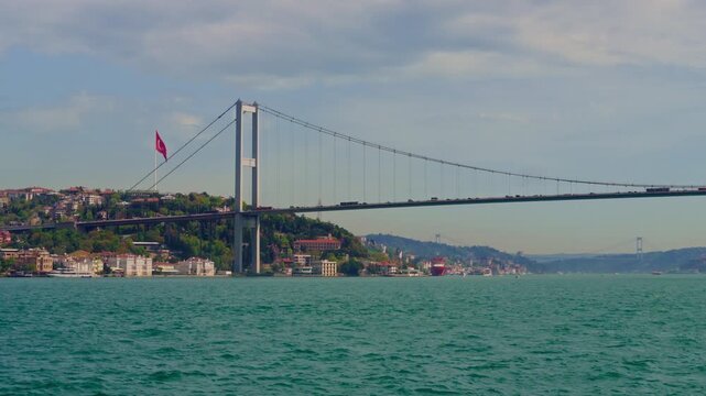 Panoramic view of the iconic Bosphorus Bridge connecting Europe and Asia with lush green hills and urban landscape under a cloudy sky in Istanbul