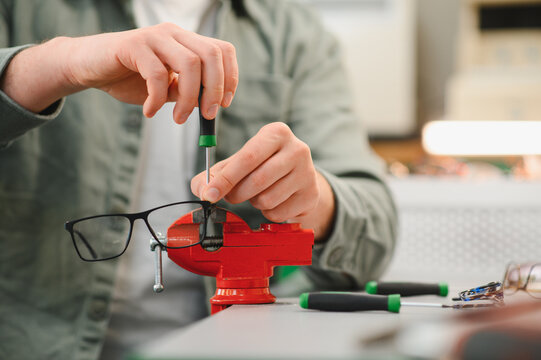 Hands repairing eyeglasses using precision screwdriver and vise