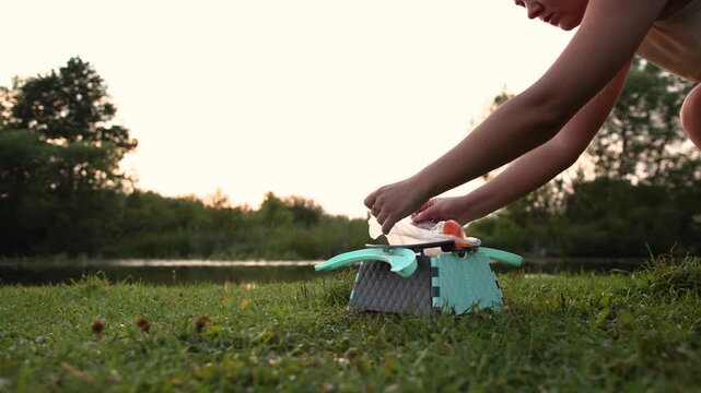 At sunset female hands collect water filled bag from portable folding plastic child toilet. Slow motion footage demonstrates practical camping sanitation beside river.