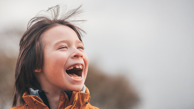 Laughing Boy in Orange Jacket Portrait Against Bright Sky