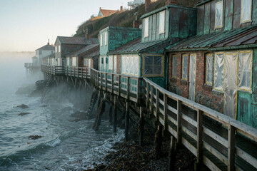 Obraz premium Weathered fishing shacks on stilts over the ocean at dawn with fog