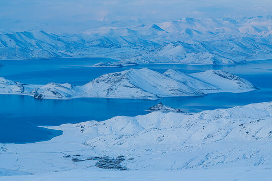 Panoramic winter scenery of Yamdrok Lake surrounded by snow-covered mountains after fresh snowfall in Tibet Autonomous Region, China. The vivid turquoise-blue waters contrast beautifully with the whit