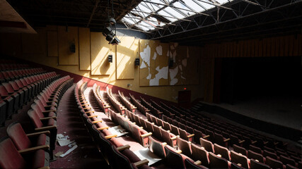 Naklejka premium Abandoned theater interior with empty red seats and peeling walls