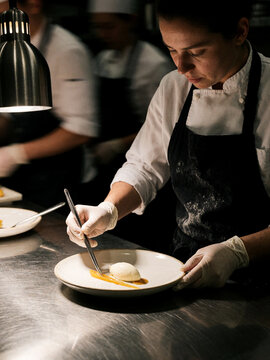 Female chef carefully plating a gourmet dessert in a professional restaurant kitchen