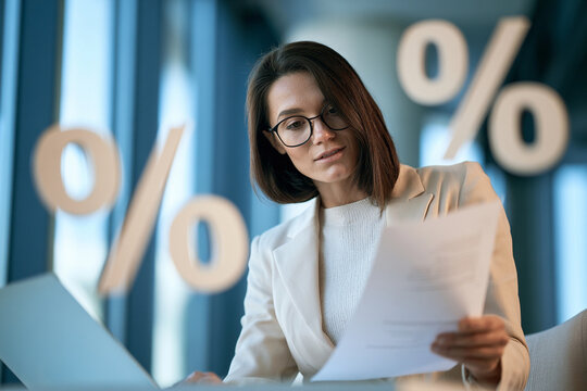 Businesswoman interest rate hikes percentage document finance office laptop glasses businesswoman reviewing document office with percentage symbol, interest rate hikes concept for finance analysis