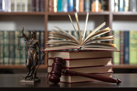 A judge's gavel and a figure of Themis against a background of books and bookshelves in an office.