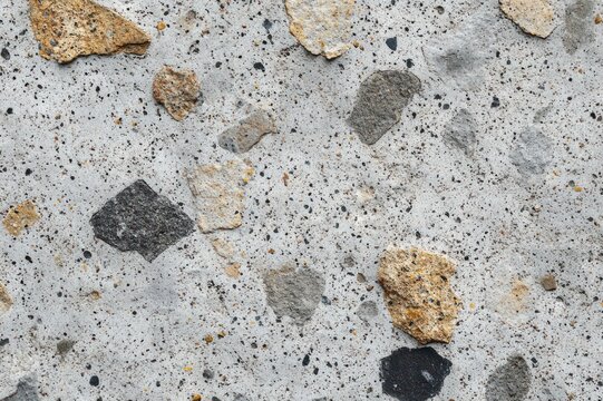 close-up of exposed aggregate concrete with scattered tan, gray, and black stones and speckled rough texture, rugged industrial and weathered mood