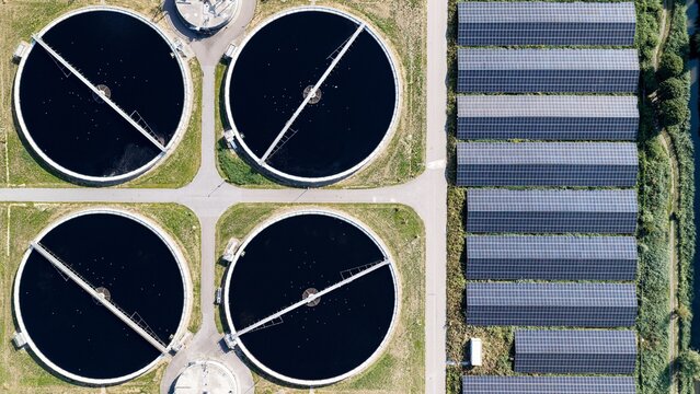 Aerial view of a wastewater treatment plant with circular sedimentation tanks and rows of solar panels in Delft, South Holland, Netherlands.