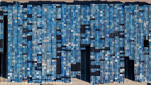 Aerial view of a large organized grid of stacked blue and black plastic crates in an industrial storage yard in Delft, South Holland, Netherlands.