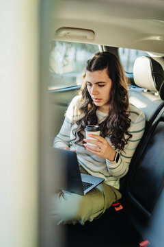 Woman working on laptop in car, drinking coffee