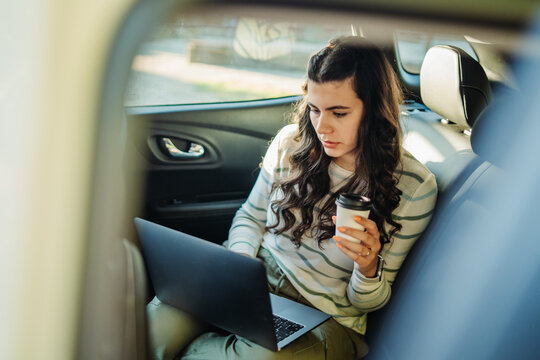 Woman working on laptop while commuting in car