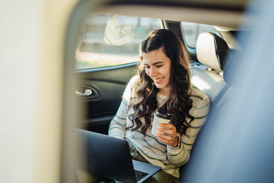 Woman working on laptop in car with coffee