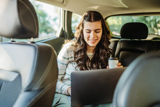 Woman working on laptop in car with coffee