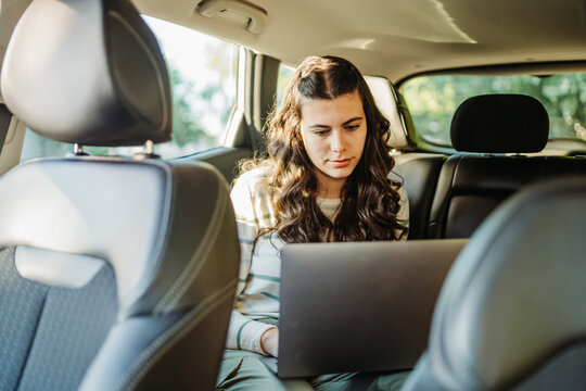 Young woman working on laptop in car backseat