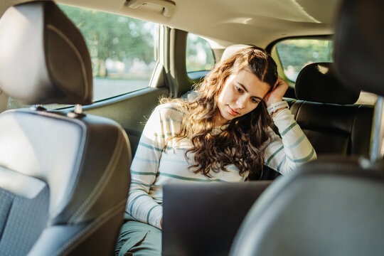Young woman working on laptop in car backseat