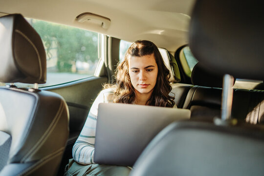 Woman working on laptop in car back seat
