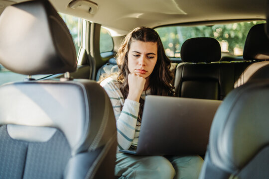 Woman working on laptop in car backseat