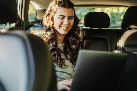 Woman smiling while working on laptop in car