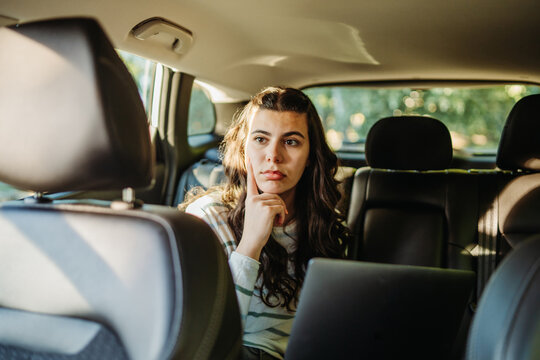 Woman thinking while working remotely in car backseat