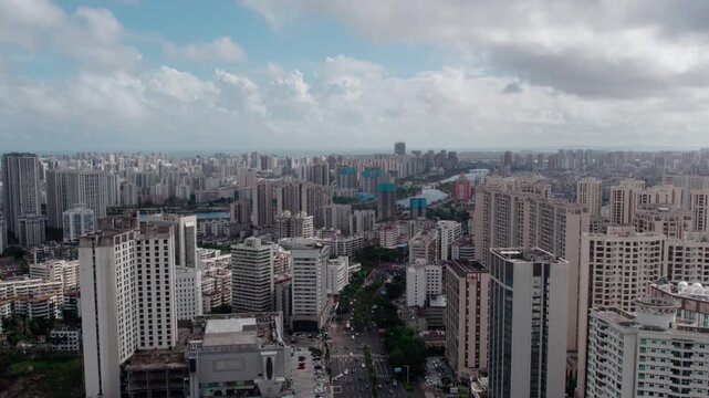 A high-angle panoramic shot of a dense urban area with numerous high-rise buildings and a winding river under a cloudy sky.