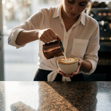 Barista pouring latte art into a ceramic cup, coffee shop scene