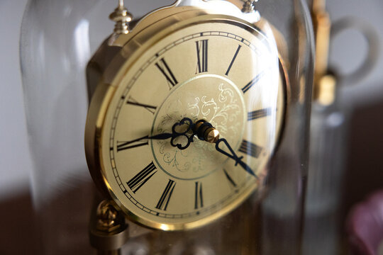 An old brass clock, time, clock face with roman numerals under a glass dome. Instrument of time, clock hand, minute handle, hour handle, watch.