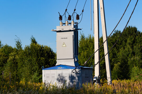 Compact electrical substation unit mounted on concrete poles for rural power supply, featuring high voltage transformers and grid cables amidst a green summer forest setting, 10 kilovolts