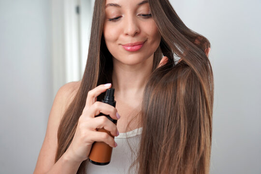 Young Woman Spraying Liquid Keratin Treatment on Her Shiny Long Hair