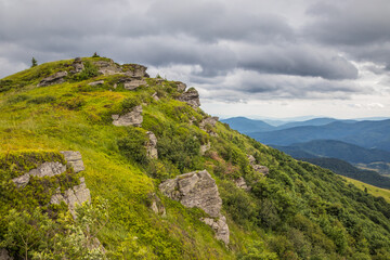 Fototapeta premium Serene landscape of a grassy hill with grey rock outcrops under a moody and cloudy mountain sky