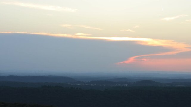 Sunset over forested hills seen from Luitpoldturm near Pirmasens, Germany. Static shot of layered ridges, distant wind turbines and orange clouds in the Palatinate Forest in summer