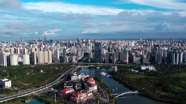 An aerial panorama of a dense modern city with a winding river, highways, and green spaces under a clear blue sky.