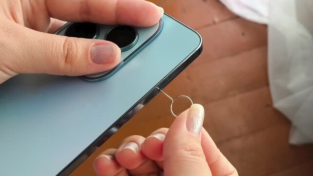 Close up of woman using SIM ejector pin to open phone SIM tray, mobile communication, smartphone setup and internet connection.