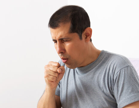 Shot of a handsome young man suffering with thecoughing as symptom for cold or bronchitis with white background