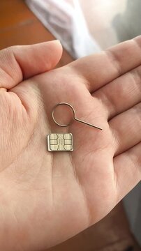 SIM card and SIM ejector tool held in hand close up, mobile connectivity, cellular network and mobile internet concept.