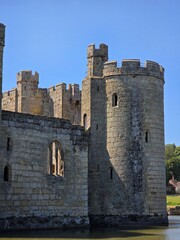 Stone castle tower and defensive wall with battlements, lancet windows, and turrets against a clear blue sky © ann_lsnk