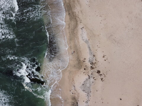 Aerial view of the coastline at Paracas with waves crashing against dark rocks on the sandy beach in Paracas, Ica, Peru.